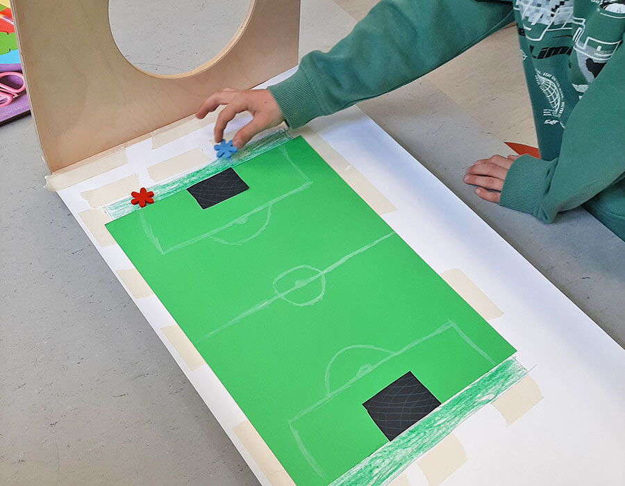 Hand eines Kindes auf einem gebastelten Papier-Fußballfeld