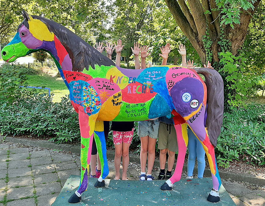 Kinder stehen hinter einer bunten Pferdestatue