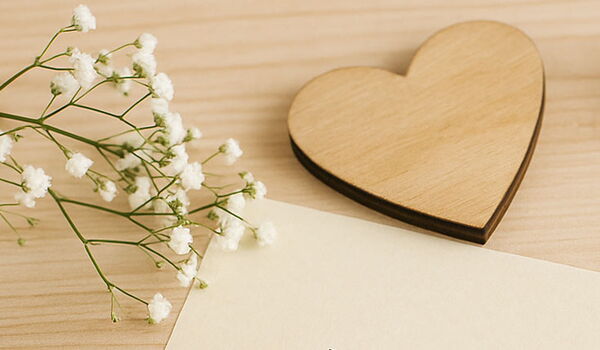 Holzherz liegt auf Schreibtisch neben einem leeren Blatt Papier und kleinen Blumen
