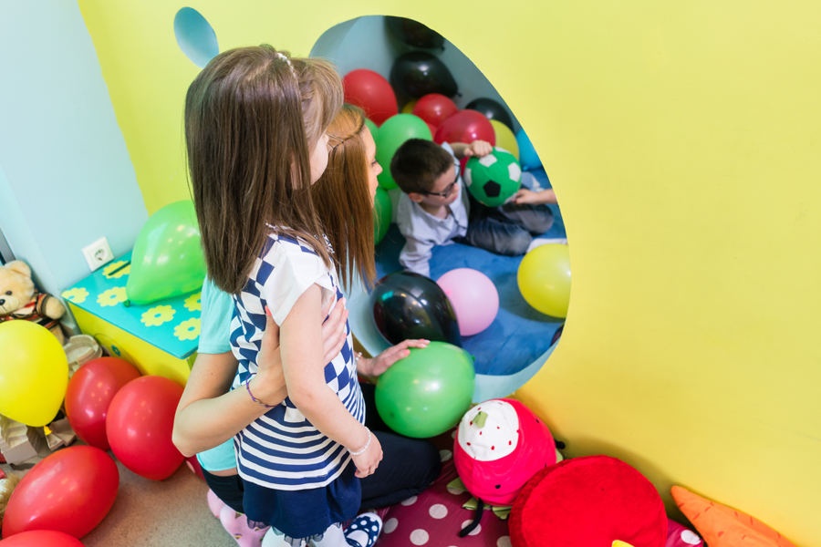 Kind mit Erzieherin im Spielparadies mit Luftballons