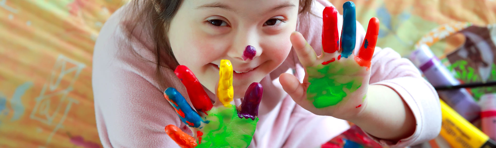 Kind mit Down-Syndrom mit Fingermalfarbe an den Händen