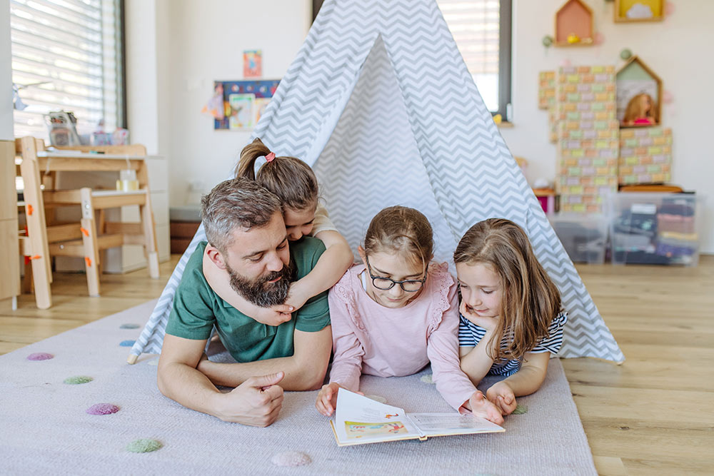 Mann liegt mit Kindern auf dem Boden und liest in einem Kinderbuch