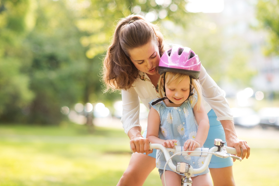 Frau hilft Mädchen mit Kinderfahrrad