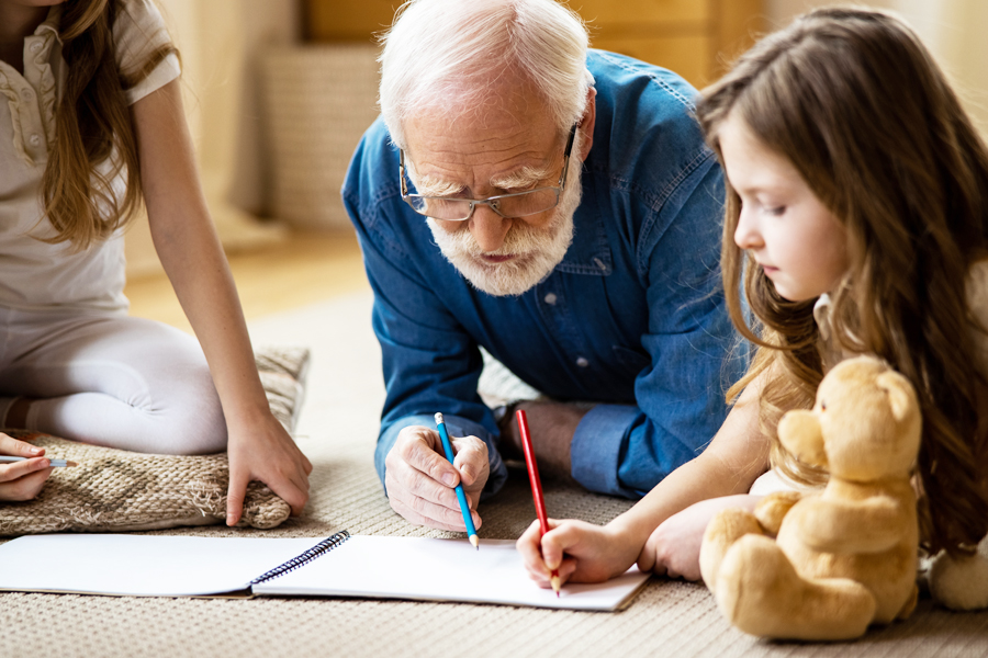 Opa liegt mit Enkelkindern auf dem Teppich und malt