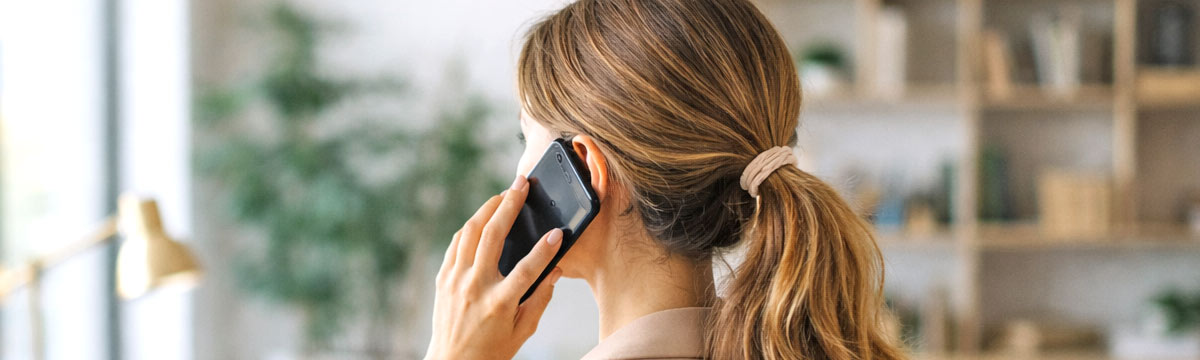 Junge Frau telefoniert stehend am Fenster vor Großstadt-Kulisse