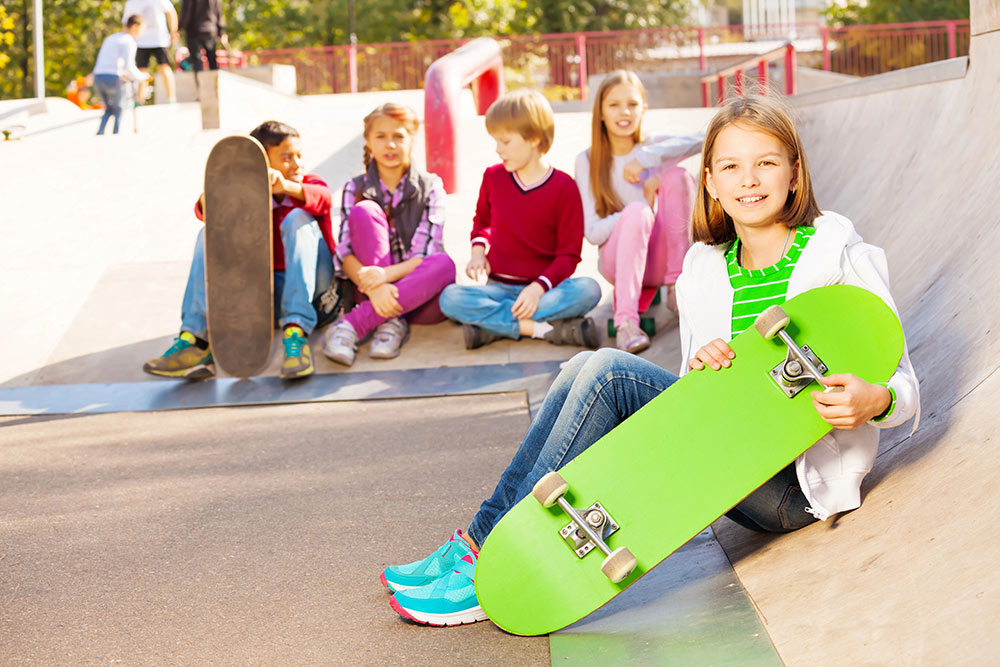Kinder sitzen mit ihren Skateboards auf einem Skaterplatz